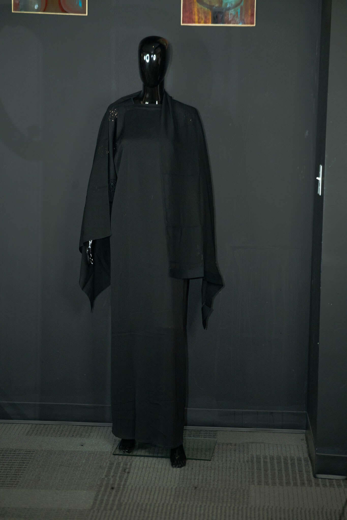 Black abaya with intricate multicolored patterns displayed on a mannequin at Oumy Beauty Studio