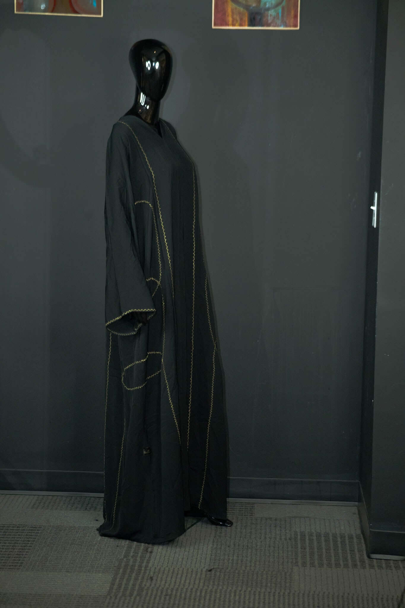 Black abaya with intricate multicolored patterns displayed on a mannequin at Oumy Beauty Studio.