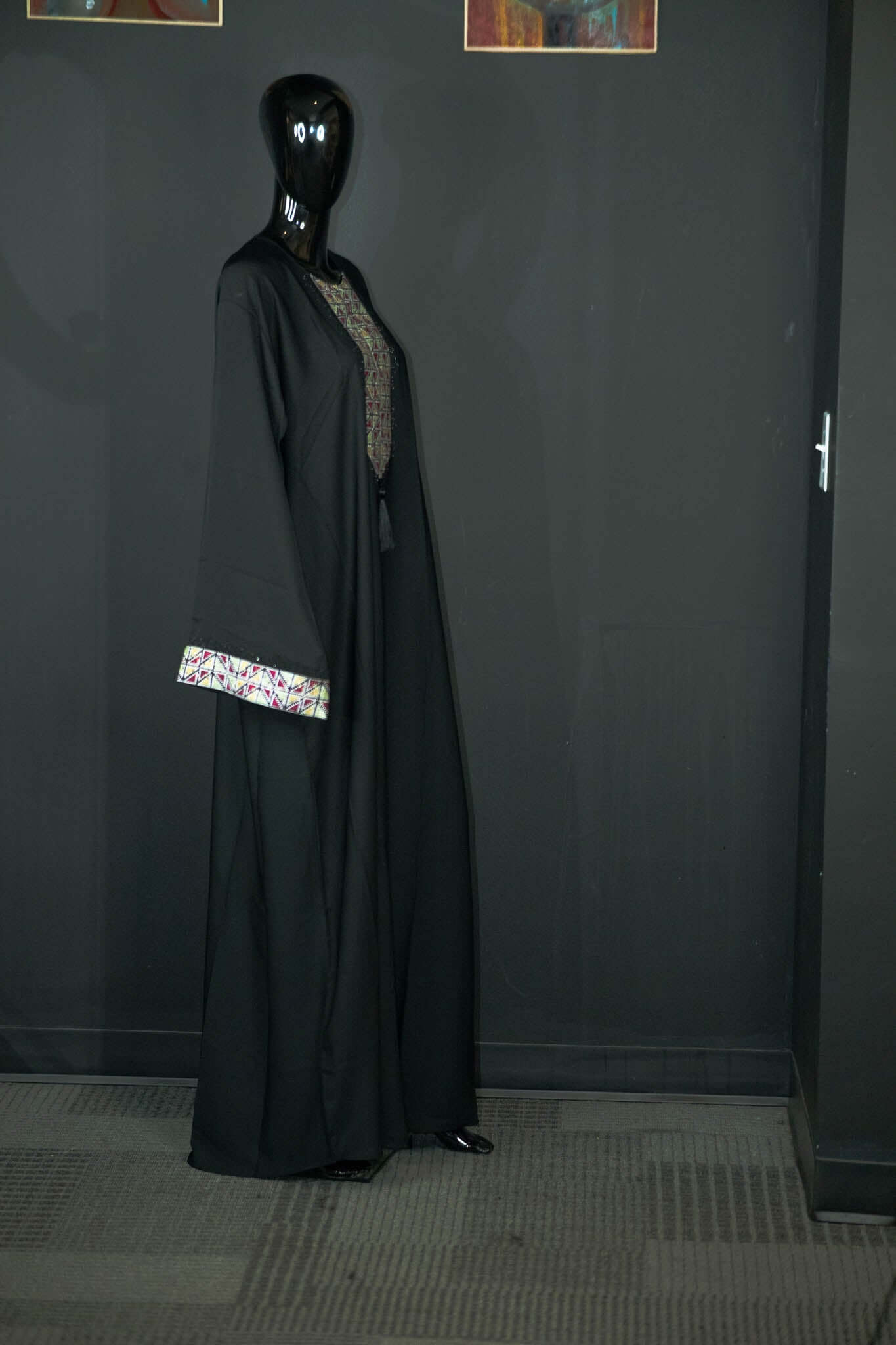 Black abaya with intricate designs from Oumy Beauty Studio, features multicolored patterns on chest and cuffs, made of silky fabric.