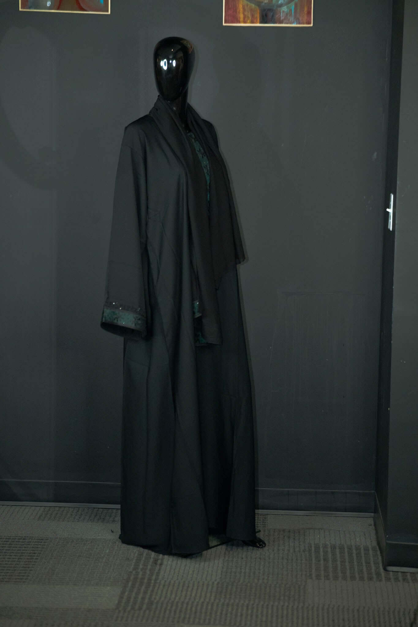 Elegant black abaya with intricate designs on display from Oumy Beauty Studio placed against a dark background.